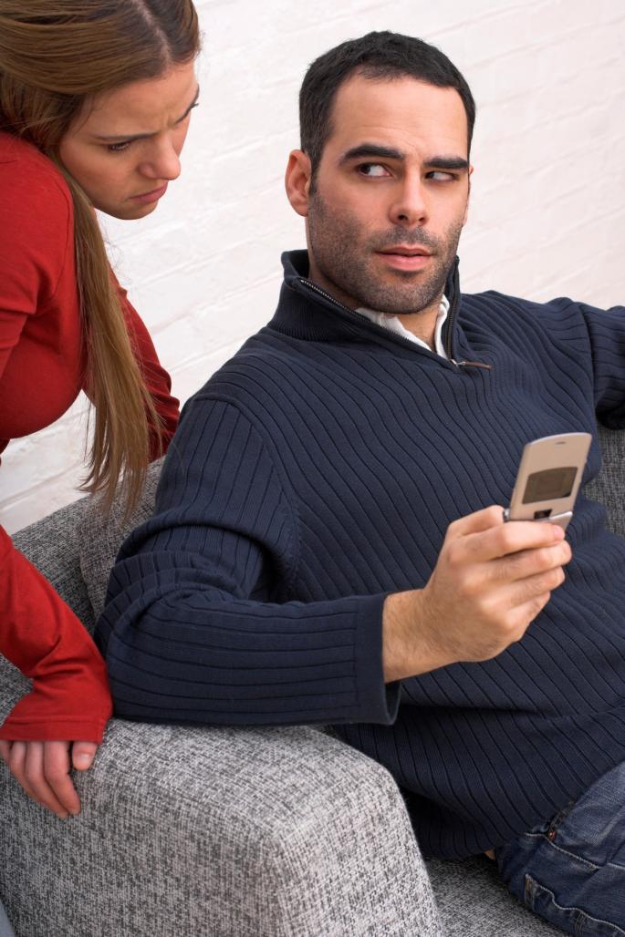 Muškarac drži telefon i gleda sumnjičavo ka ženi